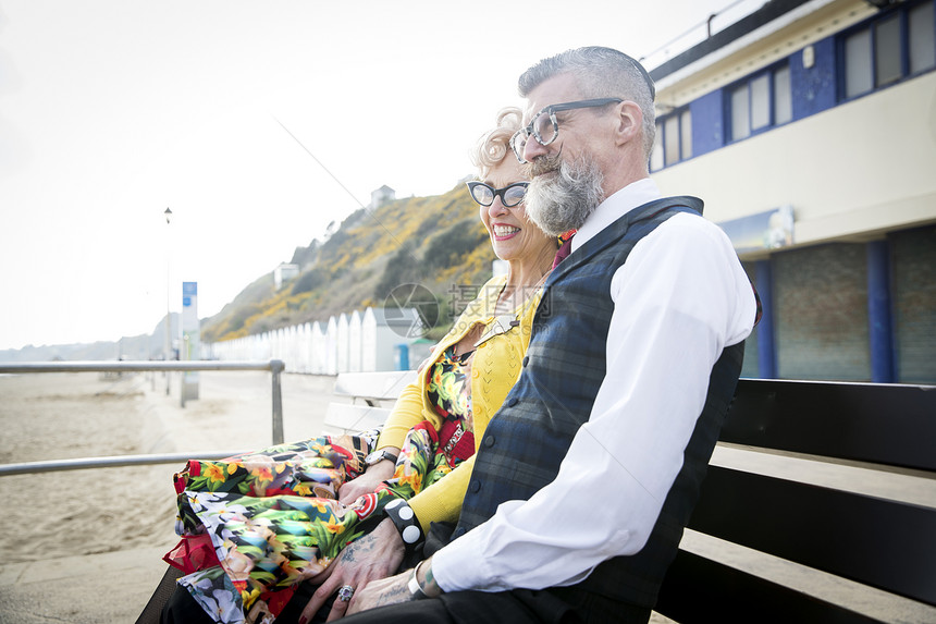 海滩长椅上打扮复古的老年夫妻在微笑图片
