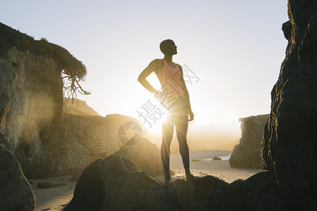 年轻女人站在海滩的岩石上看着风景海岸高清图片素材