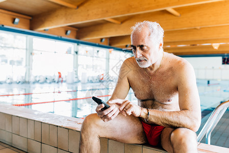 在游泳池边玩手机的中老年男性图片