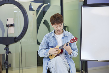 青年男性艺考学生手机直播弹奏吉他高清图片
