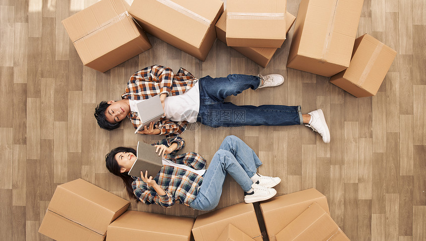 创意俯拍青年情侣躺在新家地板上看书图片