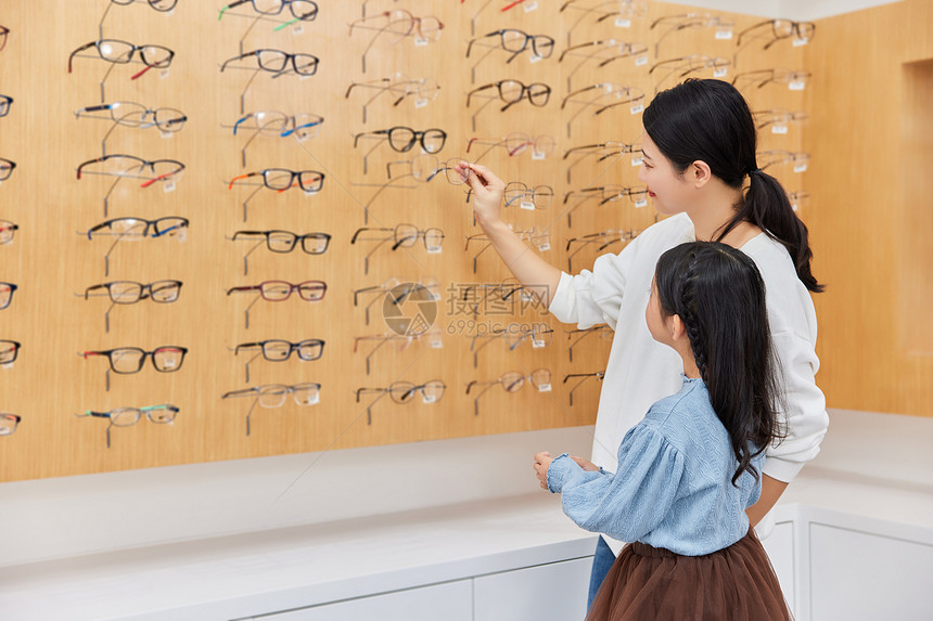 年轻妈妈和小女孩在眼镜店里挑选眼镜图片