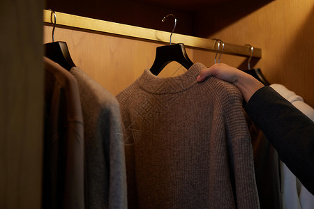 一排毛衣往衣柜里挂衣服手部特写背景