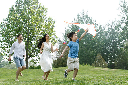 男孩在放风筝跑爱30多岁一家三口在草地上放风筝背景