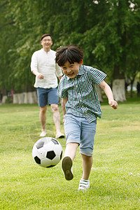 温馨园林快乐父子在草地上踢足球背景
