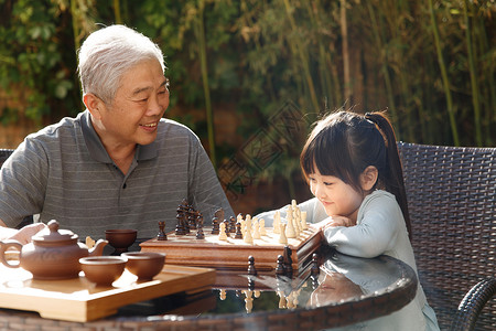 女孩在庭院里欢乐老年人象棋祖父和孙女在庭院里下棋背景