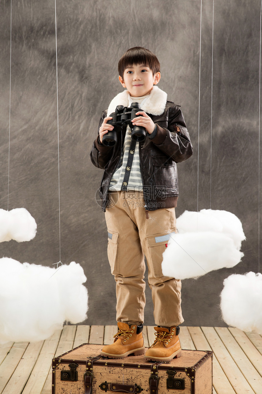 可爱的儿童快乐男孩拿着望远镜站在行李箱上图片