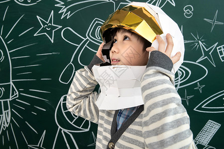 孩子火箭戴着航天员头盔的小男孩站在黑板前背景