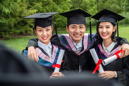 户外三个穿着学士服的大学生搂在一起学位帽高清图片素材