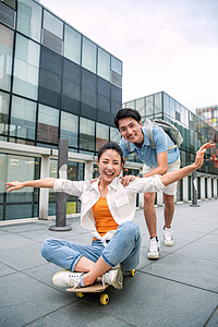 广场上的人男子向前推着坐在滑板上的女友背景