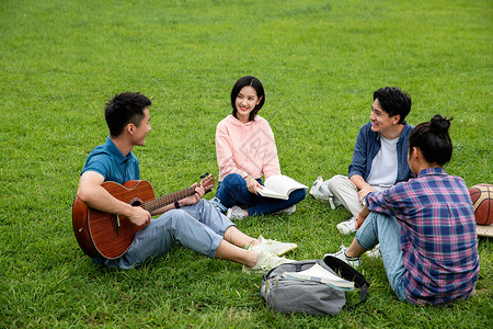 成人教育书包弹奏快乐的大学生在草地上弹吉他唱歌图片