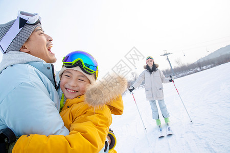 快乐滑雪场上抱在一起的父子和滑雪的母亲高清图片