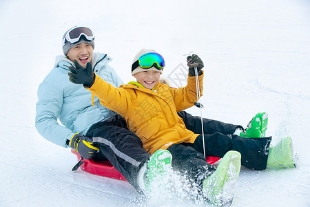 拉着绳子的男孩兴奋的父子坐着雪上滑板滑雪背景