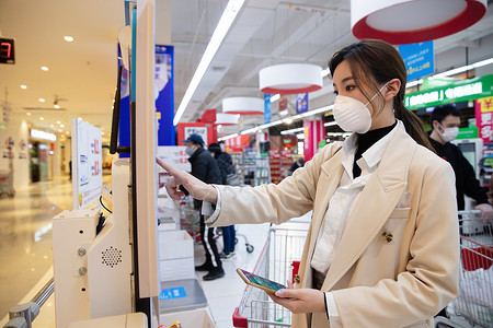 手机防护套戴口罩的青年女人在超市用手机付款背景