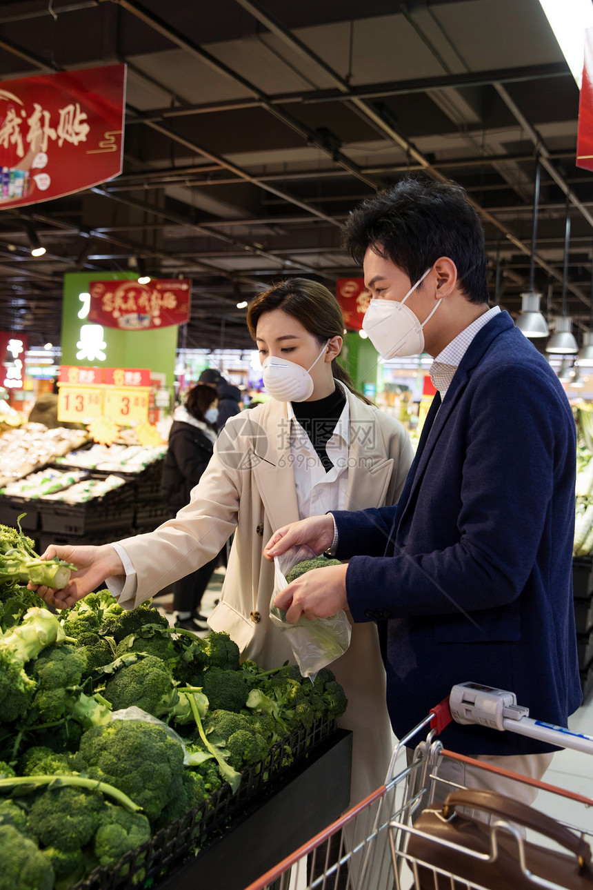 户内摆放健康保健青年夫妇戴口罩在超市挑选蔬菜图片