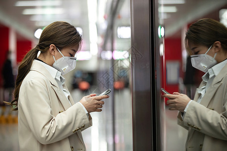 通讯设施戴口罩的年轻女人站在地铁站台上背景