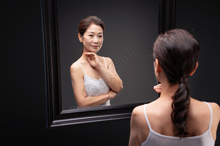 优雅的中年女欣赏镜子中的自己自信高清图片素材