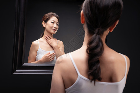 做优雅女人中老年女人对着镜子做颈部护理背景