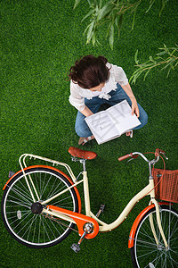 白昼盘着腿坐自由坐在草地上看书的青年女人图片