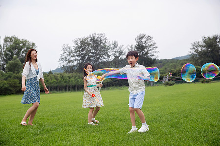 东亚家庭相伴妈妈带着两个孩子在草地上快乐玩耍高清图片