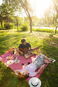 欢乐25岁到29岁轻松坐在公园里弹吉他的幸福情侣高清图片
