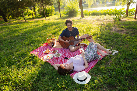 躺着约会的情侣无忧无虑休闲不看镜头在公园里弹吉他的幸福情侣背景