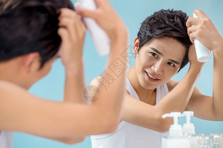 亚洲美发用品欢乐照着镜子给头发喷啫喱的年轻男人图片