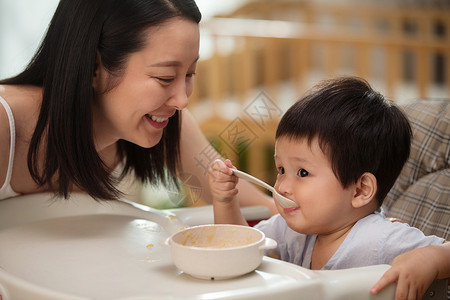 坐椅子上男孩年轻妈妈喂餐椅上的宝宝吃饭背景