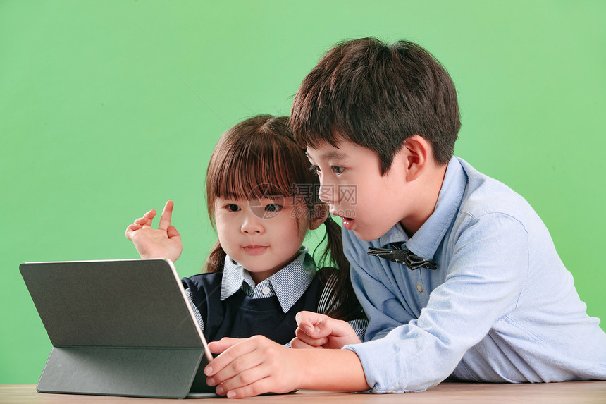 绿色背景天真儿童两个小伙伴使用平板电脑图片