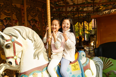 骑木马的小孩游乐园两个小女孩在玩旋转木马背景