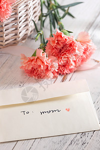 母亲节粉色花瓣桌上的康乃馨花和信封贺卡背景