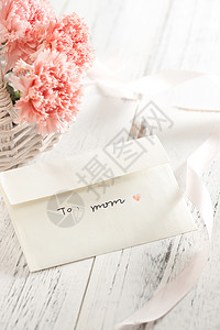 母亲节粉色花瓣桌上的康乃馨花和信封贺卡背景