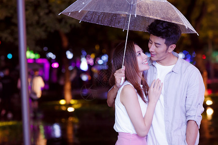 举着伞情侣下雨天夜里一起逛街的情侣背景