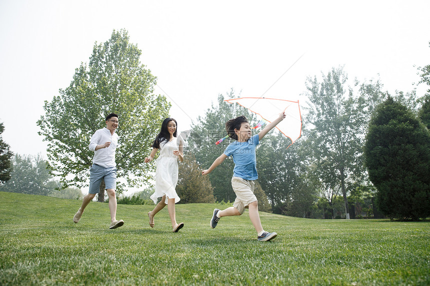 东方人放风筝独生子家庭一家三口在草地上奔跑图片