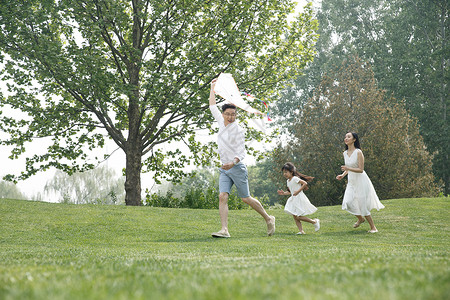 双亲家庭户外女孩一家三口在草地上放风筝图片