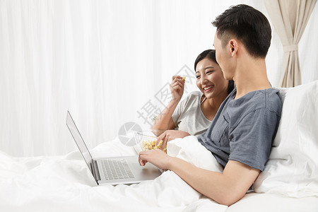 亚洲人幸福青年夫妇青年情侣坐着床上看电脑图片