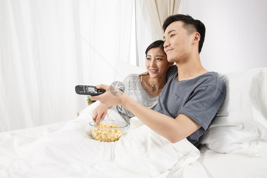 家庭生活摄影愉悦青年情侣坐着床上看电视图片