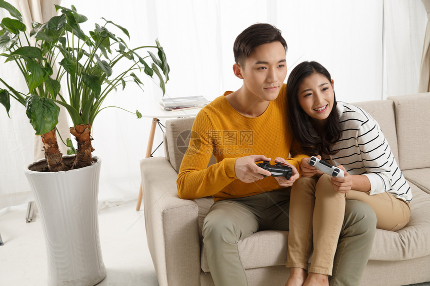 亚洲人相伴刺激青年情侣坐着沙发上玩游戏图片