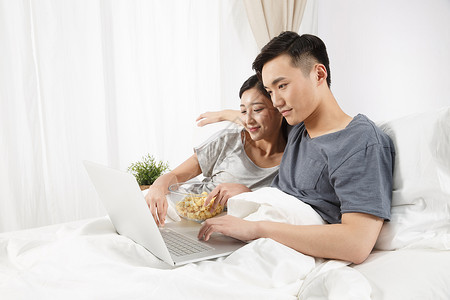 休闲生活仅成年人快乐青年情侣坐着床上看电脑图片