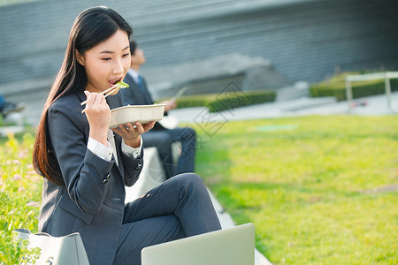 吃盒饭的人商务女性坐着户外边吃饭边工作背景