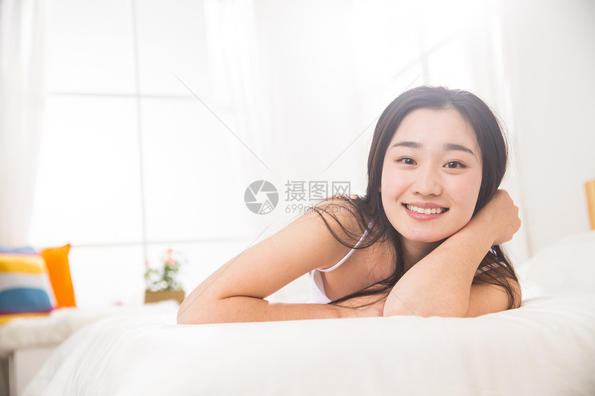 早晨微笑纯洁青年女人趴在床上图片