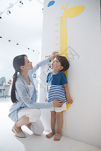 教师尺三角板幼师家居尺青年女人在为小男孩测量身高背景