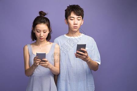 紫色背景不理的不看镜头各自玩手机的青年情侣图片