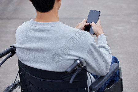青年男性外出坐轮椅使用手机特写背景图片