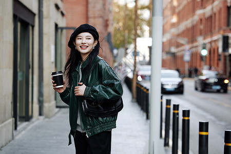 手拿咖啡行走街头的青年女性背景图片