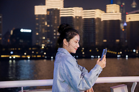 夜晚在游轮船上用手机自拍的旅游女生高清图片