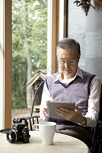 老年男性独自居家窗边看电脑喝茶背景图片