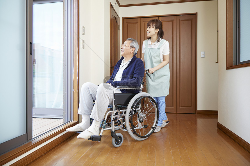 护工在室内推行坐在轮椅上的老人图片