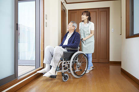护工在室内推行坐在轮椅上的老人背景图片