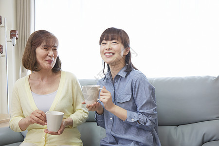 女儿和母亲在沙发上喝下午茶笑容高清图片素材